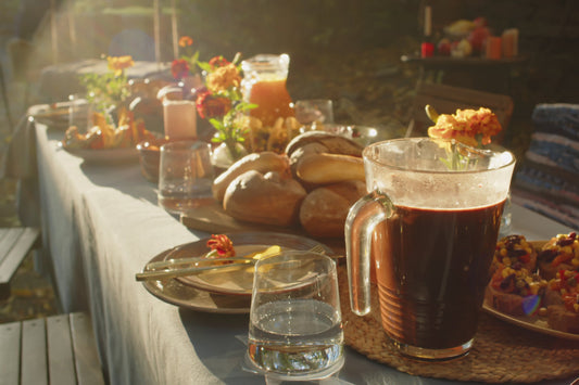 A large picnic table stretches away, laden with fresh fruit, bread, juice and flowers, and bathed in bright sunlight.